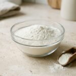 Wie wird Proteinpulver hergestellt: weißes Proteinpulver in einer Schale neben einem Messlöffel